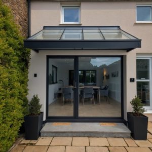 Modern glass roof canopy above sliding patio doors with geometric planters and a minimalist garden setting.